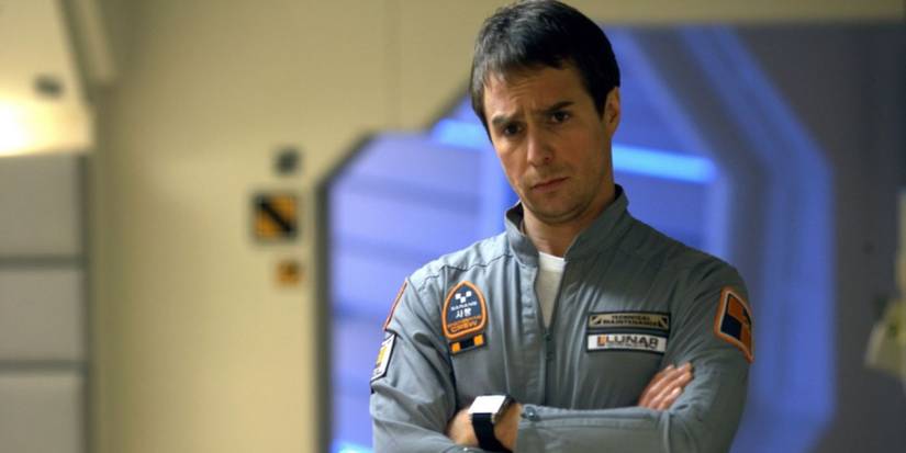 Sam Rockwell as Sam Bell, stands with his arms crossed, in Moon
