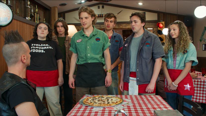 Still from the new series Minimum Wage, showing teen employees of a pizza shop standing around a cus...
