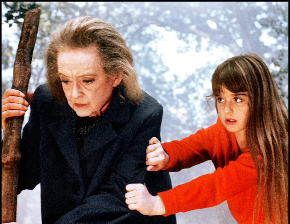 Bette Davis holds a walking stick as a young Kyle Richards in a red sweater grips her arm in a foggy forest