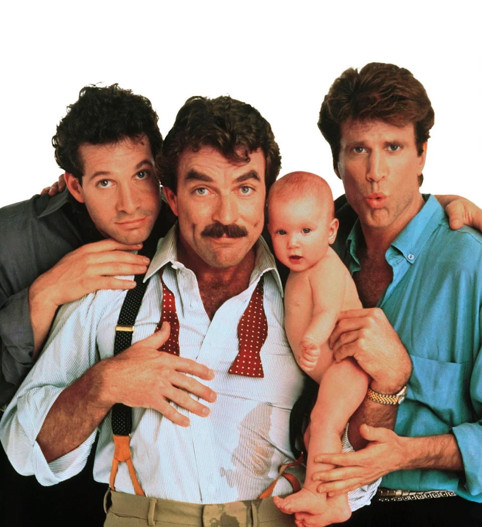 Steve Guttenberg, Tom Selleck holding a baby and Ted Danson pose together in a publicity photo for Three Men and a Baby